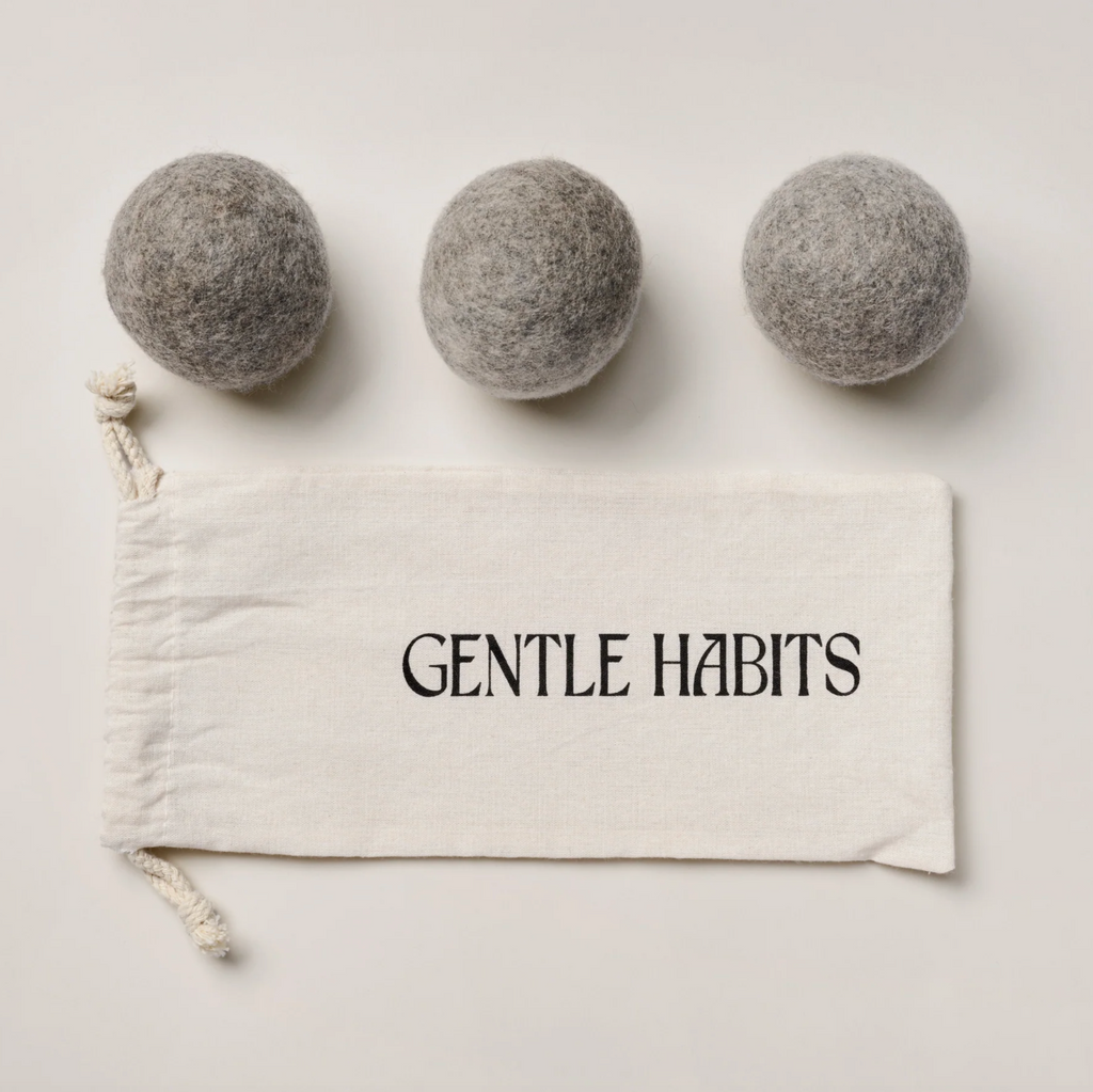 Three gray wool dryer balls on a white background with a 'Gentle Habits' drawstring bag.