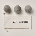 Three gray wool dryer balls on a white background with a 'Gentle Habits' drawstring bag.