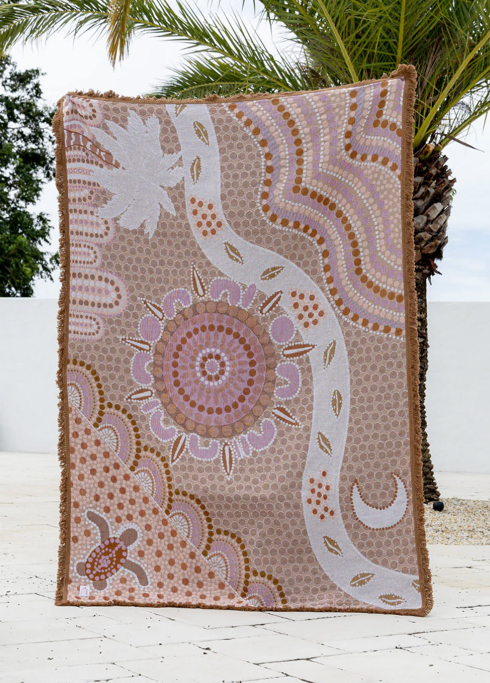 Decorative blanket with a intricate pattern on a wooden surface with palm trees in the background