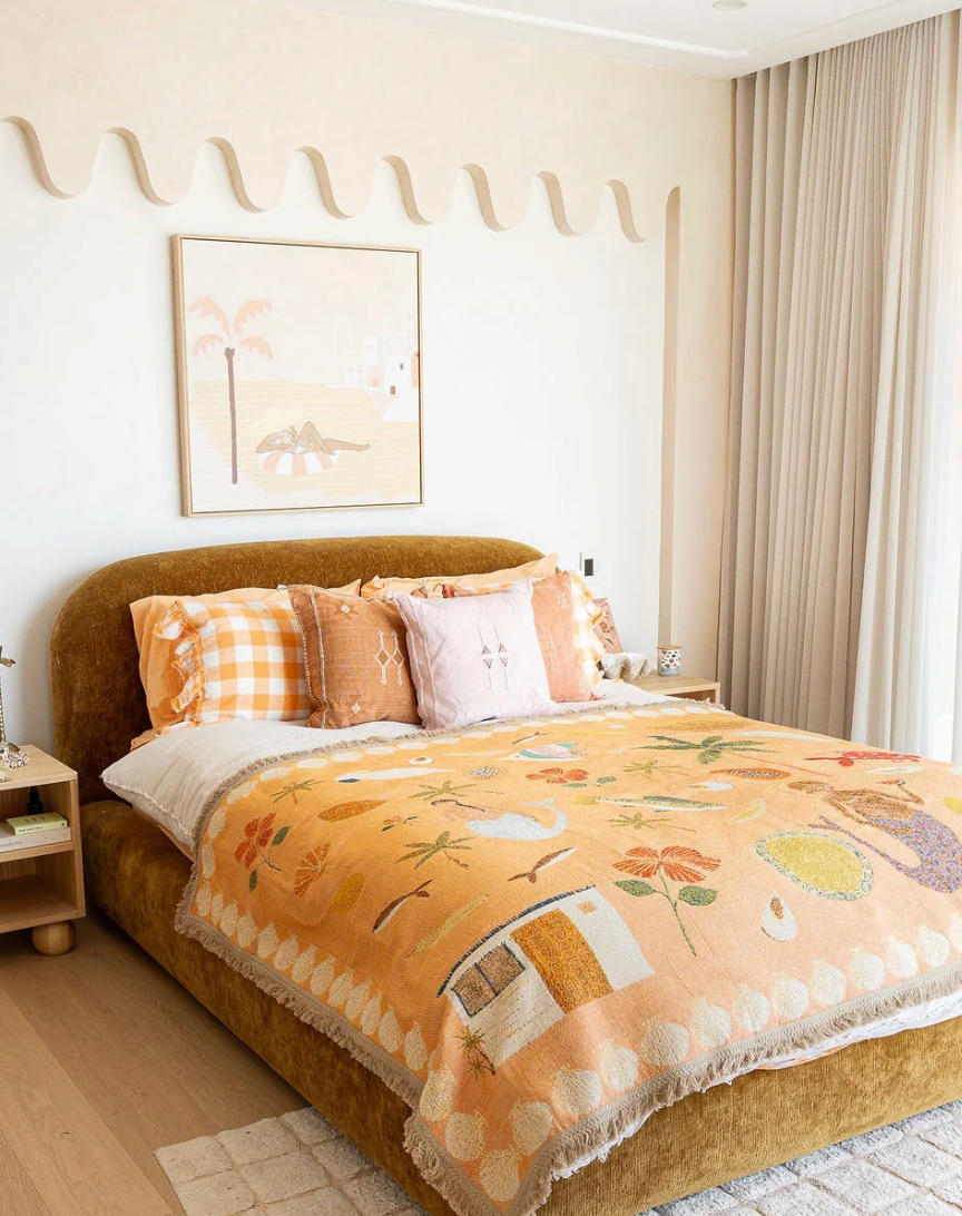 Bedroom with a bed covered in a floral blanket, pillows, and a framed picture on the wall.