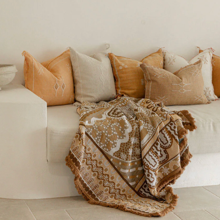 Beige and brown patterned blanket draped over a white sofa with decorative pillows.