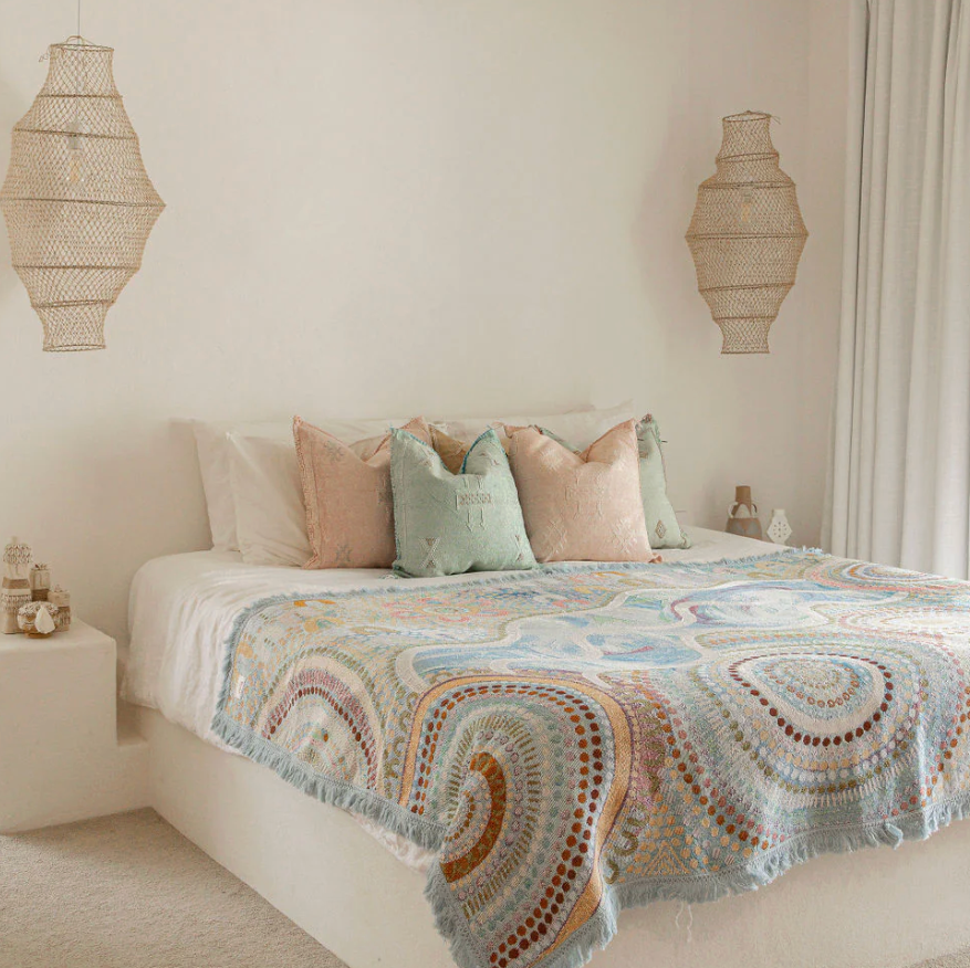 Bedroom with a bed featuring a patterned quilt and decorative pillows, with wicker lamps on the walls.