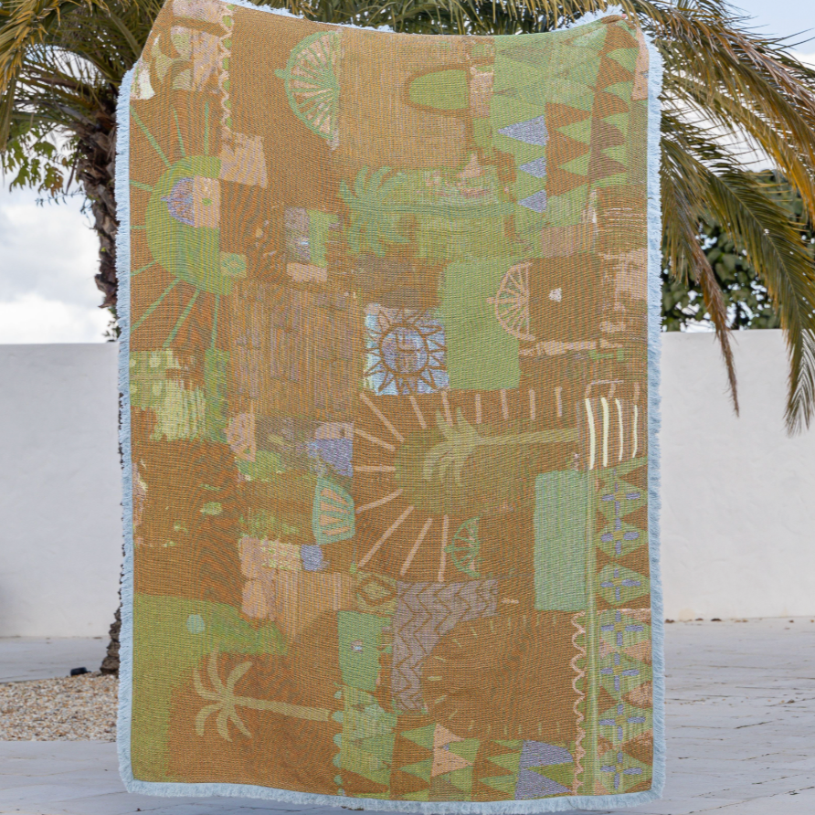 Decorative blanket with geometric pattern on a wooden surface with palm trees in the background