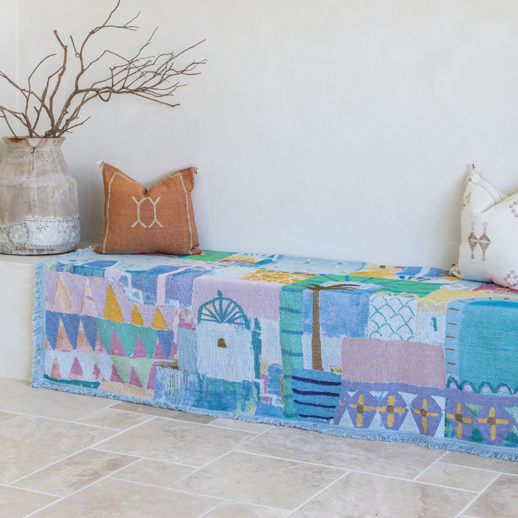 Colorful quilt with geometric patterns on a bench against a white wall.