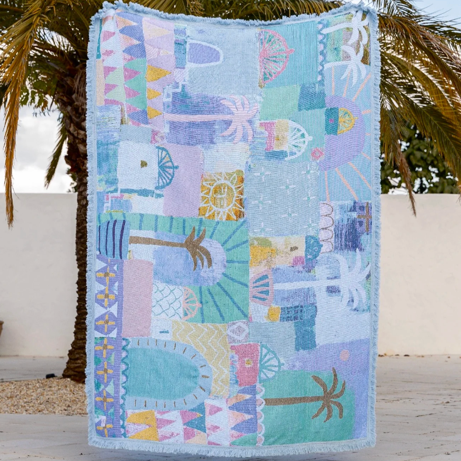 Colorful quilt with geometric patterns displayed outdoors against a palm tree.