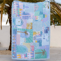 Colorful quilt with geometric patterns displayed outdoors against a palm tree.