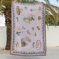 Decorative blanket with mermaid and shell patterns on a wooden surface with palm trees in the background
