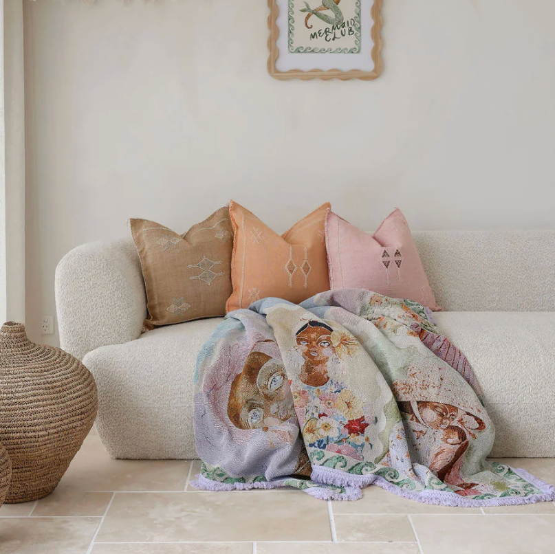 Decorative throw blanket with embroidered designs on a beige sofa with patterned pillows.